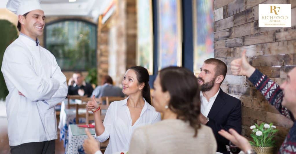 A caterer is talking to a group of people. The caterer is taking notes and asking questions, making sure that the food will be personalized to the group's preferences.