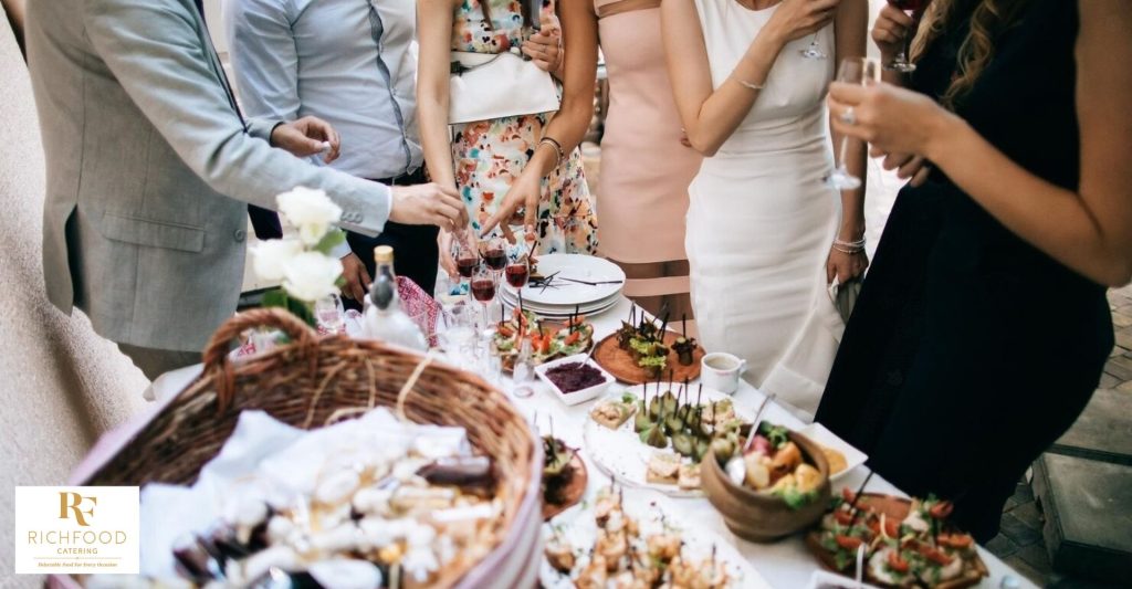 A group of people are standing around a buffet table, looking at the food.