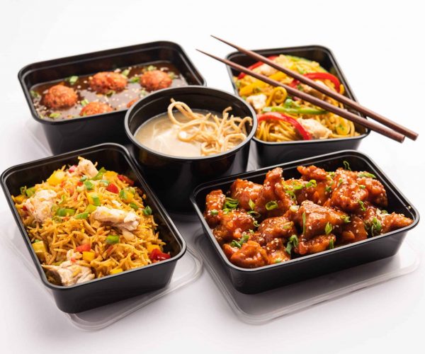 Group of home delivered Indo Chinese food in plastic packages, containers or boxes containing schezwan noodles, fried rice, chilli chicken, manchurian and soup. Online food ordering concept in India